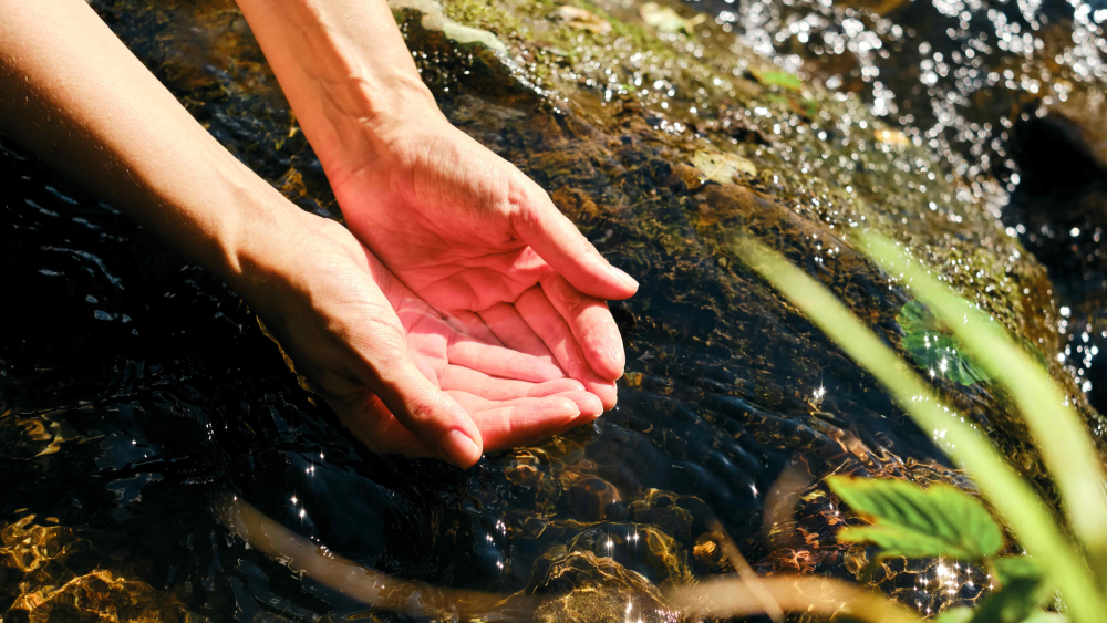 Zwei Hände schöpfen klares Wasser mit Spurenelementen aus einem Fluss.